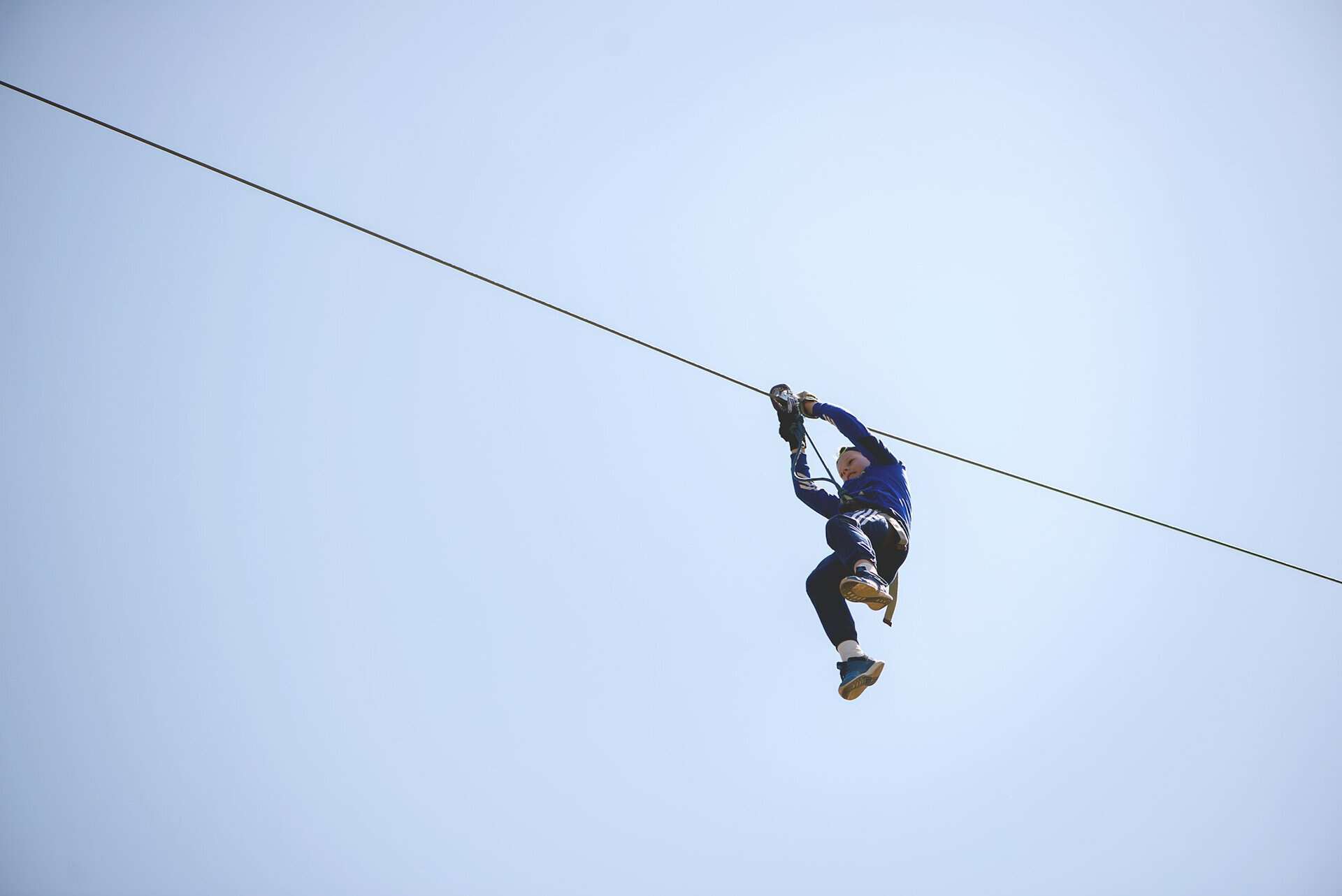 Rear view of young boy riding on zip line against blue sky